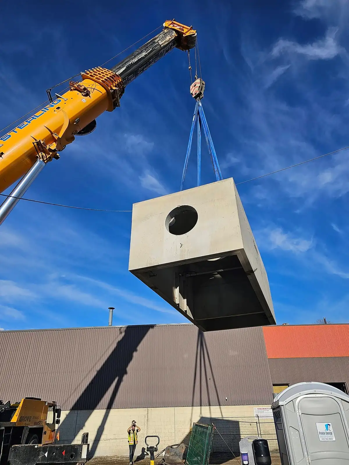 Precast concrete vault lifted by mobile crane over the excavation