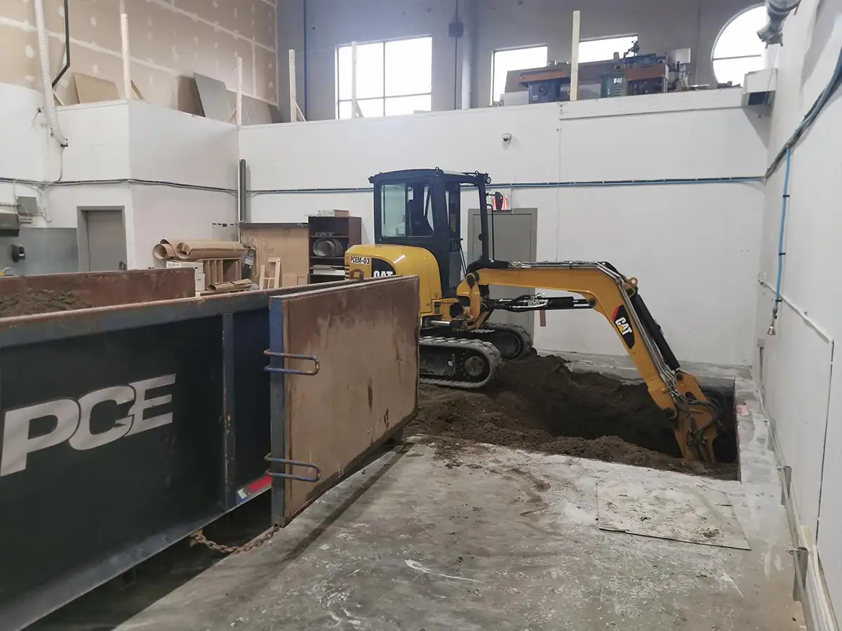 Compact excavator working inside the building beside a PCE bin